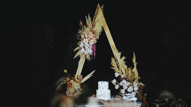 Beautiful wedding cake decorated with dried flowers in the evening near the arch, slow motion.