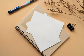 Postcard, white paper on a brown notebook with pen and dried flowers on orange background. Mockup stationary template. 
