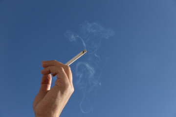 cigarette in man hand against a blue sky. close up. High quality photo