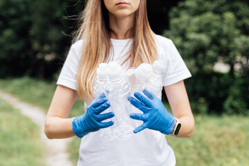 Young caucasian woman cleaning-up public park or forest of plastic garbage. Volunteer picking up plastic bottle in woods. Green and clean nature, avoid pollution, be friendly to the environment and