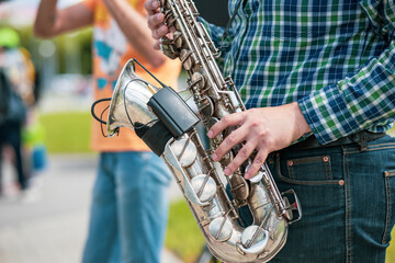 a street musician plays the saxophone in the street, a plaid shirt and hands