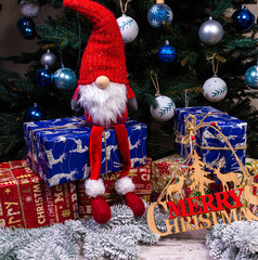 The inscription winter from a tree on a New Year's. On the spruce branches against the background of a snow cover are New Year's blue, white balls with spruce cones and a box with a gift. Christmas