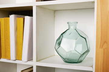 Round faceted green glass vase on a square white bookshelf. Glass object to decorate the space....