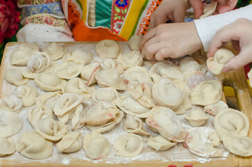 The children's hands, soiled with flour, neatly lay out handmade, freshly ravioli, meat dumpling or pelmeni on cutting boards. Teaching children to cook homemade food, joint work. selective focus.