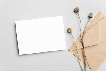 Blank wedding invitation card mockup with envelope and dry plant decor. Flat lay, top view, copy space