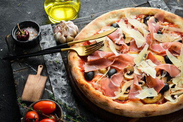 Delicious homemade pizza with prosciutto and Parmesan cheese. Home delivery of food. On a black stone background.
