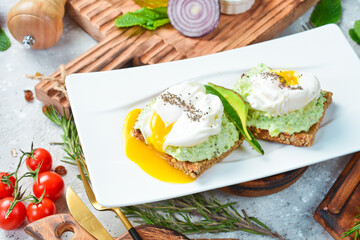 breakfast Sandwich with poached egg and avocado. On a white plate. On a gray stone background. Restaurant menu.
