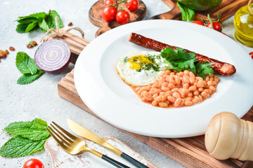 Breakfast. Eggs with sausage and beans. On a white plate. On a gray stone background. Restaurant menu.
