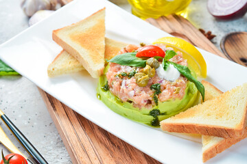 Tartar. Salmon, avocado and onion tartare with bread toast. On a white plate. On a gray stone background. Restaurant menu.