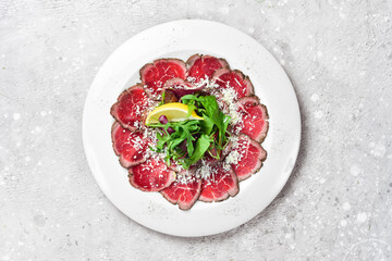 Veal carpaccio with lemon and arugula. On a white plate. On a gray stone background. Restaurant menu.