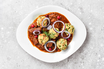Veal baked in tomato sauce with meatballs. On a white plate. On a gray stone background. Restaurant menu.