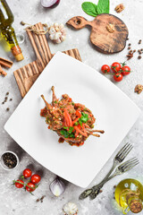 Quail baked in tomato sauce with vegetables. On a white plate. On a gray stone background. Restaurant menu.