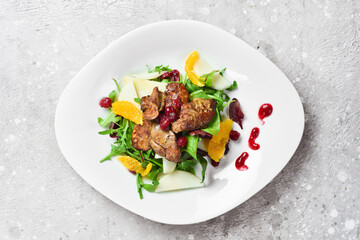 Warm vegetable salad with goose liver and cranberry. On a white plate. On a gray stone background. Restaurant menu.