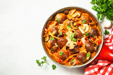 Meatballs with mushrooms in tomato sauce in a frying pan.