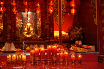 Bangkok : temple bouddhiste dans le quartier chinois avec de nombreux lampions rouges et autels où brulent des bougies  devant des statues de bouddhas dorés 