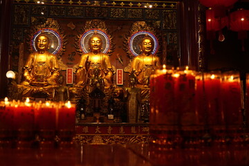 Bangkok : temple bouddhiste dans le quartier chinois avec de nombreux lampions rouges et autels où brulent des bougies  devant des statues de bouddhas dorés 