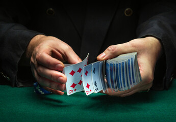 A professional dealer or croupier quickly shuffles playing cards in a club at a green table with...