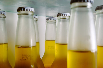 Cold beer bottles, closeup, cooling glass bottles with yellow alcohol liquid in the fridge before the party.
