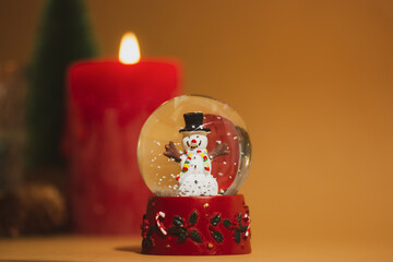 New Year's glass toy, snow globe with cheerful snowman inside and snowflakes falling. Home decor, red candlelight, a gift for winter holidays. Cozy Christmas atmosphere. Happy New year 2023 wallpaper.
