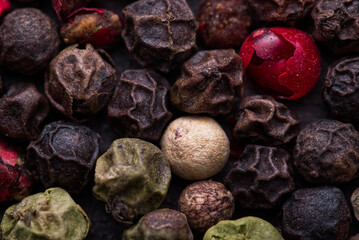 Pepper of four colors (black, red, green and white pepper) macro details. Combination of all peppers color types in one picture on dark wood table.