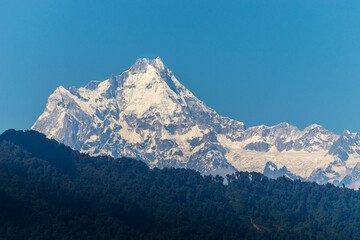 Kangchenjunga, ook wel gespeld als Kanchenjunga, Kanchanjangha en Khangchendzonga, is de op twee na hoogste berg ter wereld. De besneeuwde top van de berg torent hoog boven het dichte groene bos uit.
