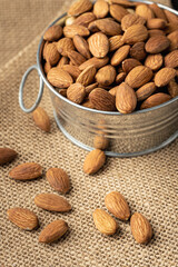 Metal bowl full of almonds on a sackcloth. Pile of nuts stacked together randomly on the burlap background. Healthy nutrition concept