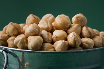 A pile of peeled hazelnuts in a metal bowl on the green background Healthy nutrition concept. Traditional rustic agricultural background. Copy space for a free text