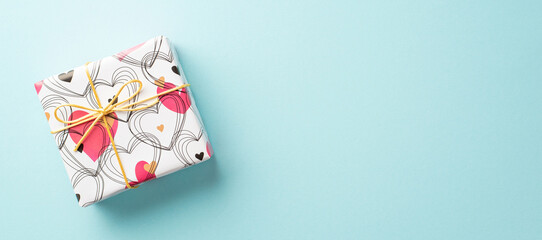 Valentine's Day concept. Top view photo of giftbox in wrapping paper with heart pattern on isolated pastel blue background with empty space