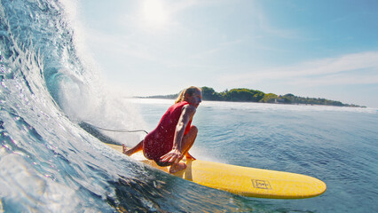 Woman surfer in red suit surf the wave on the yellow longboard in the Maldives