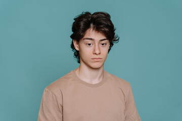 Upset handsome schoolboy tired looks down standing against turquoise studio backdrop. Unhappy guy...