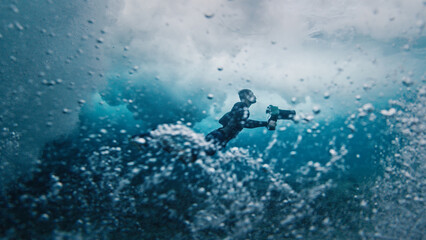 Fototapeta na wymiar Underwater view of the surf photographer diving under the wave with camera