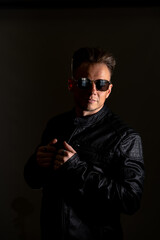 Portrait of handsome male. Sexy stylish man dressed in a leather jacket and sunglasses. Fashion hipster male isolated on grey background in studio