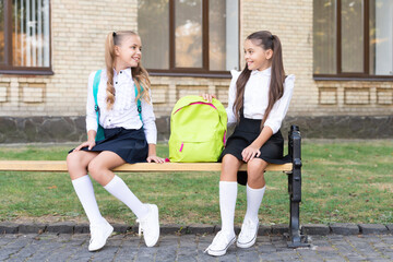 two school girls friends sit on bench with backpack together