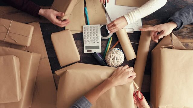 Hands, brown paper and small business production, wrap and box package for shipping, ecommerce logistics and delivery in startup. Closeup top view, group of people and packaging distribution of stock