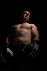 Portrait of muscular handsome topless male wearing boxing gloves isolated against a black background