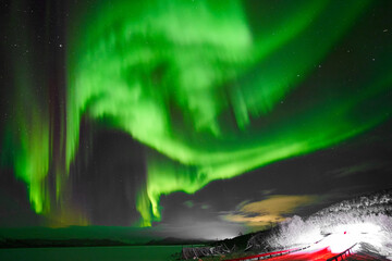 Dancing northern lights within the Arctic Circle in Lapland, Finland, next to a frozen lake and scenic drive in winter.