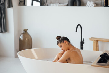 Young woman hugs her legs while sitting in the bath - 556130690