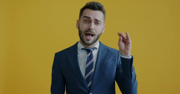 Portrait of bored and annoyed businessman saying bla bla bla and making blabbing hand gesture on yellow background. People and communication concept.