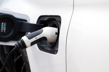 Power cable is connected to the charger of the electric vehicle close up. Charging an electric car in the parking lot