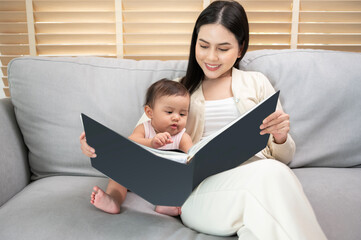 Fototapeta premium Beautiful mother reading a book to baby girl at home