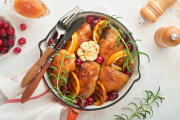 Baked chicken thighs with orange, cranberry and spicy herbs rosemary servered in frying pan on light background. Festive Christmas Dinner Concept menu. Top view. copy space