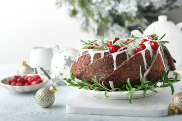 Christmas chocolate bundt cake. Traditional Christmas fruit cake with white glaze, cranberries and rosemary on white stand with Christmas decoration. Winter baking at Xmas or New Year. Copy space.