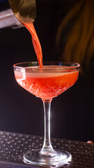 Red cocktail is poured into a glass