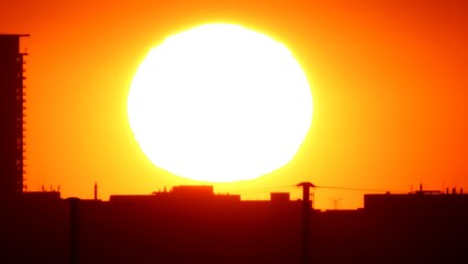 Fototapeta premium Sunset sun setting behind American downtown skyline silhouette. Epic sunset and city landmark buildings. Red and orange sun set dusk at yellow sky.