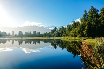 Reflections in Lake Mathieson surrounded by natural bush and forest and Southern Alps mountain range
