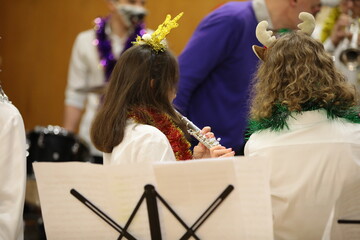 Girl musician with Christmas tinsel on clothes playing the flute at the lesson of the school student orchestra