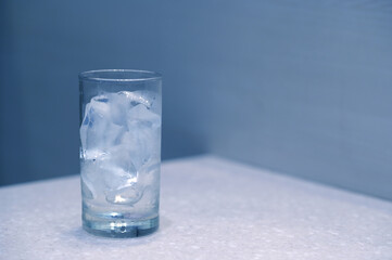 The ice in the glass is melting on the dining table. Cool tones.