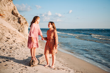 Two happy laughing teen caucasian barefooted girls wearing airy dresses holding their hands and...