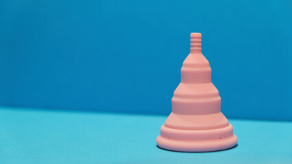 Copa menstrual rosa plegable en un fondo azul con copy space