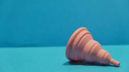Copa menstrual rosa plegable tumbada en un fondo azul con copy space